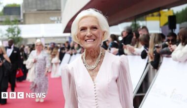 Dame Mary Berry smiles at the camera on the red carpet of the Bafta awards ceremony. She has short white hair and wears a long-sleeved pale pink dress with a pearl necklace around her neck.