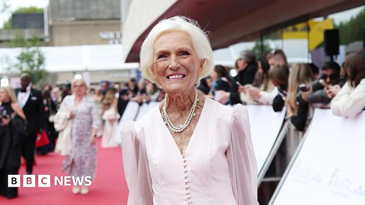 Dame Mary Berry smiles at the camera on the red carpet of the Bafta awards ceremony. She has short white hair and wears a long-sleeved pale pink dress with a pearl necklace around her neck.