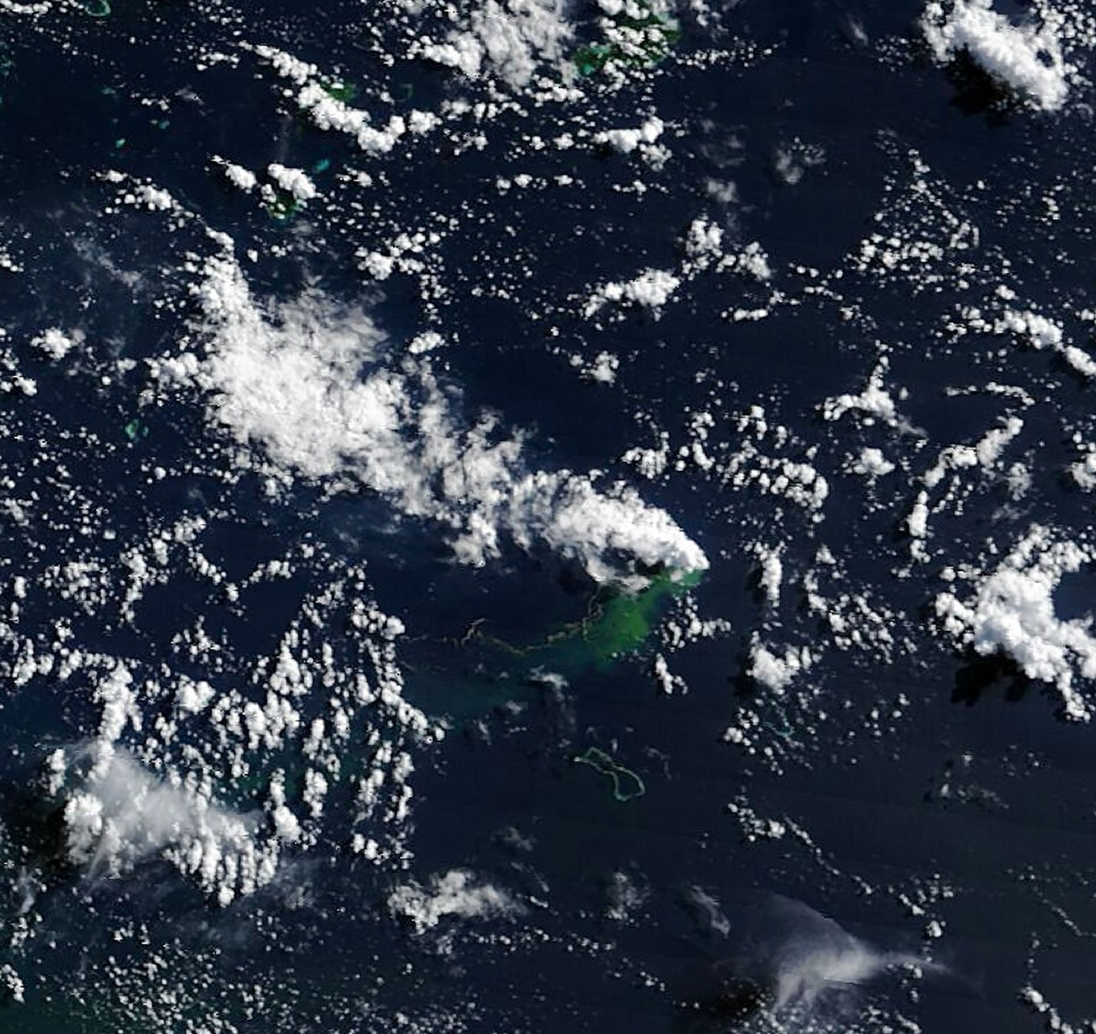 A long gray line extends west and joins with a patch of discolored green water and a cloud-like volcanic plume near the center of the image.