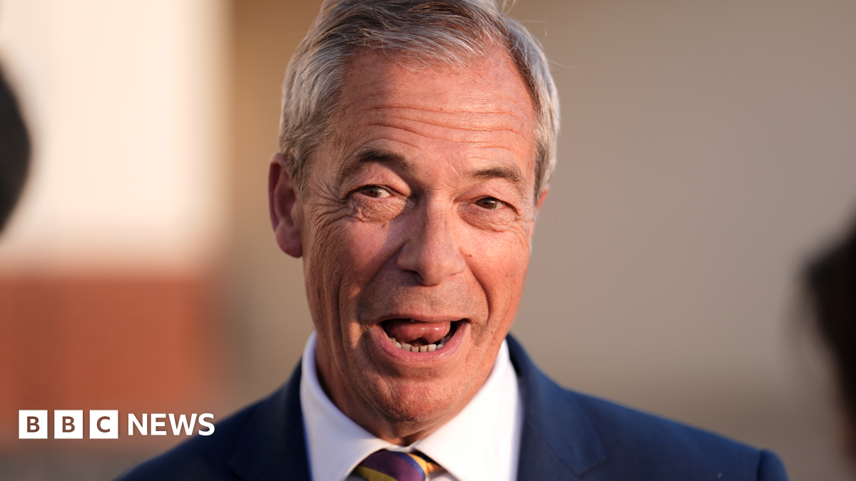Nigel Farage has short grey hair and his mouth is open as he speaks to reporters, who are not pictured. He is wearing a blue suit jacket and a white shirt.