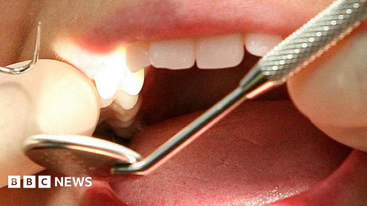 A patient's mouth being examined by a dentist who is wearing white gloves.