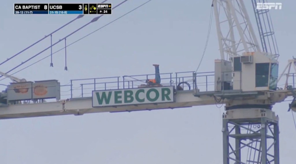 A construction worker exercising on top of a Webcor sign at a Cal Baptist vs. UCSB game.