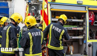 A group of firefighters in uniform grab equipment from the fire engine.