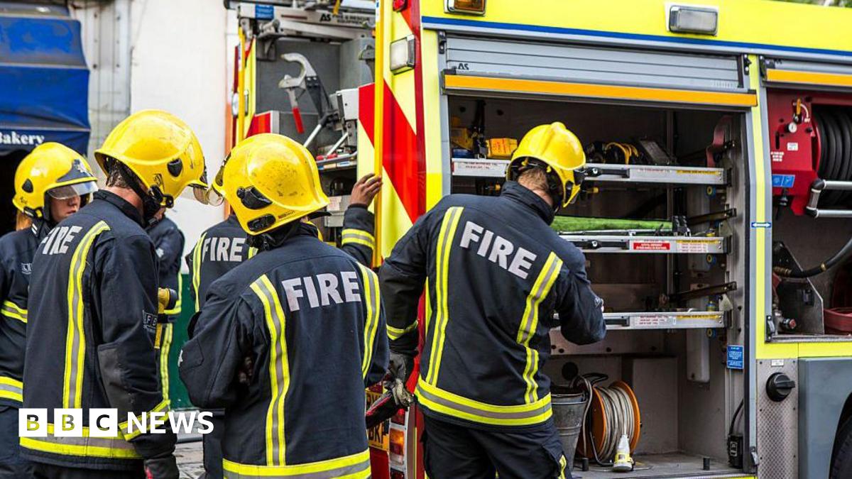 A group of firefighters in uniform grab equipment from the fire engine.