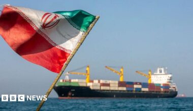 A BBC map of the Strait of Hormuz region, showing the narrow strait between The Gulf to the west and the Gulf of Oman to the east. The north of the strait is the coast of Iran and the United Arab Emirates and Oman are to the south. Bandar Abbas is highlighted in red on the Iranian coast at the narrowest point of the strait. The map also labels Dubai and Abu Dhabi in the UAE on The Gulf coast. A small inset map shows the location of the region within the Middle East and between Africa and Asia.