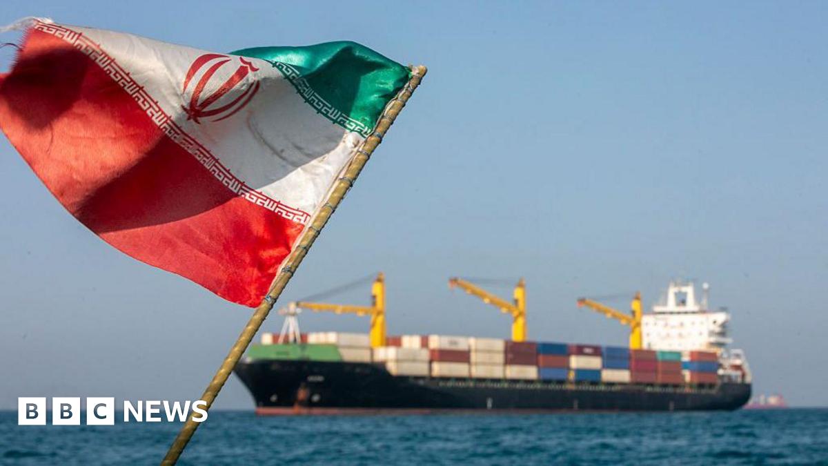 A BBC map of the Strait of Hormuz region, showing the narrow strait between The Gulf to the west and the Gulf of Oman to the east. The north of the strait is the coast of Iran and the United Arab Emirates and Oman are to the south. Bandar Abbas is highlighted in red on the Iranian coast at the narrowest point of the strait. The map also labels Dubai and Abu Dhabi in the UAE on The Gulf coast. A small inset map shows the location of the region within the Middle East and between Africa and Asia.
