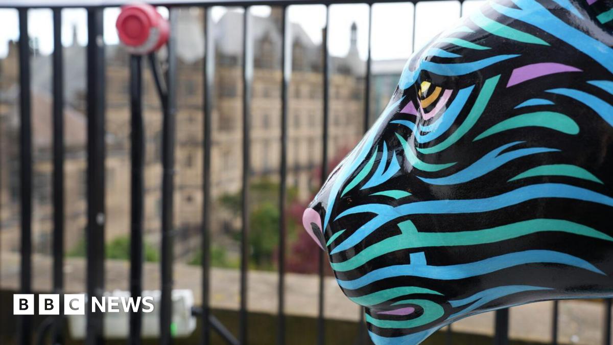 A decorated lion sculpture with blue and purple stripes is situated infront of black railing