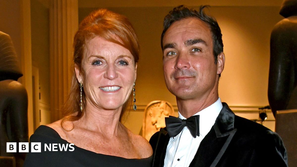 Sarah Ferguson in black dress with her hair up stands next to Manuel Fernandez who wears a black velvet jacket, white shirt and bow tie. They are both smiling at the camera.