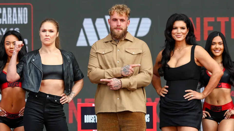 Jake Paul between Ronda Rousey and Gina Carano on stage