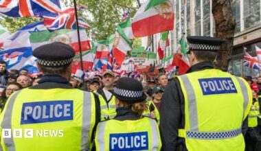 Rear view of three police officers with crowd waving a selection of flags before them
