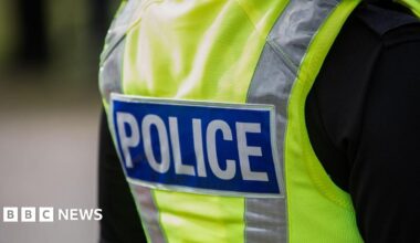Close up of the back of a police officer, wearing a black t shirt and a high vis police vest