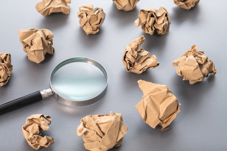A magnifying glass resting on a plain surface amongst numerous crumpled paper balls.