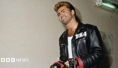 George Michael wearing a black jacket with a white BSA logo on the left side.