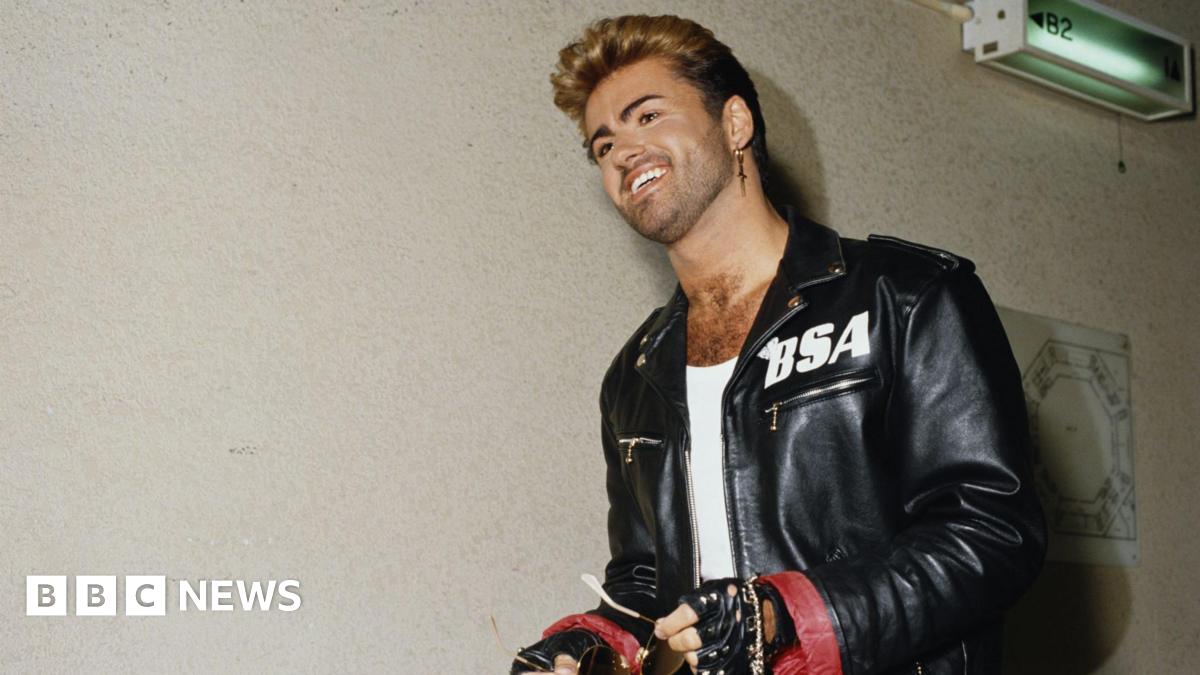 George Michael wearing a black jacket with a white BSA logo on the left side.