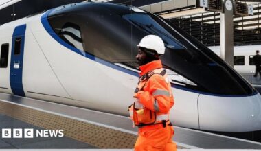 HS2 worker in a tunnel with a tunnel boring machine in front. He is wearhing an orange high-vis jacket and a blue hard hat