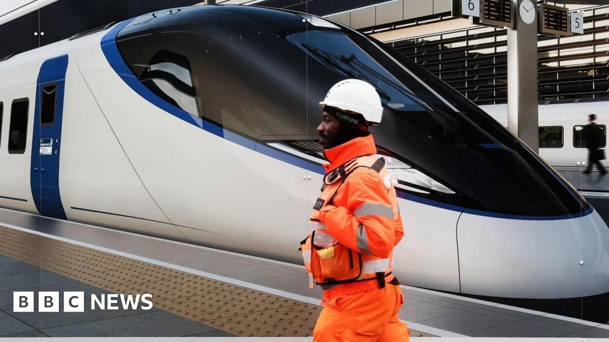 HS2 worker in a tunnel with a tunnel boring machine in front. He is wearhing an orange high-vis jacket and a blue hard hat