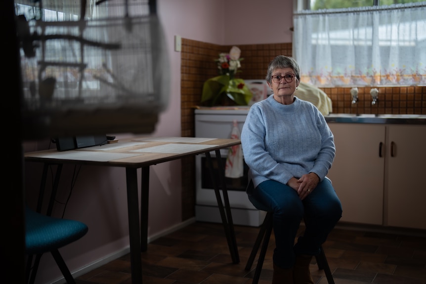 A woman in a grey jumper sits in her ktichen