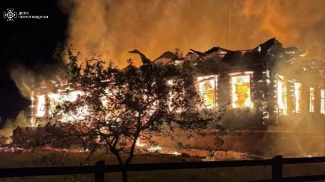 A fire rips through a single storey building. Flames can be seen in its windows and on the floor around the property. Smoke rises above it