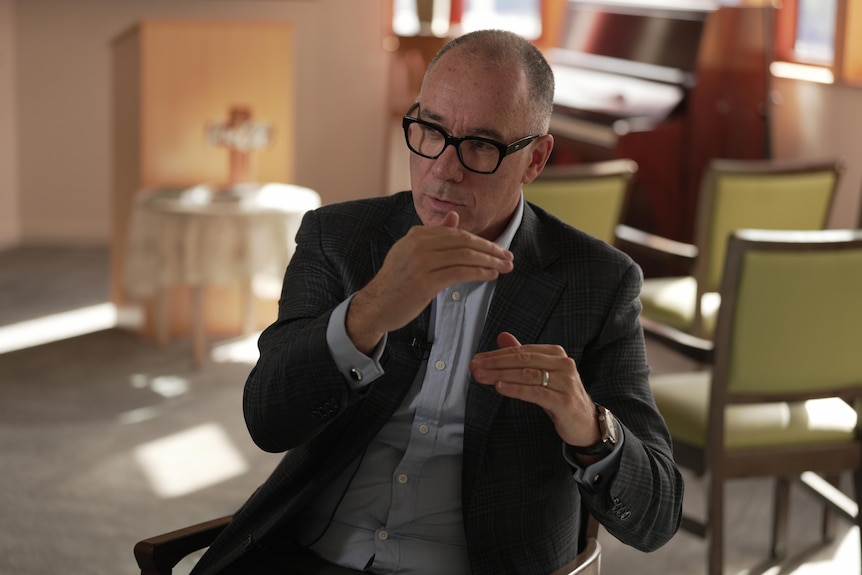 A man in a suit and glasses uses his hands to speak.