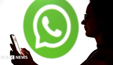 A teenager poses for a photo while holding a smartphone in front of a Whatsapp logo