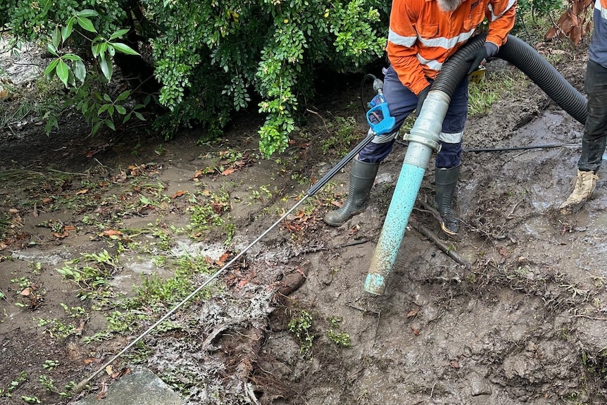 A worker in hi-vis holding a pipe in mud
