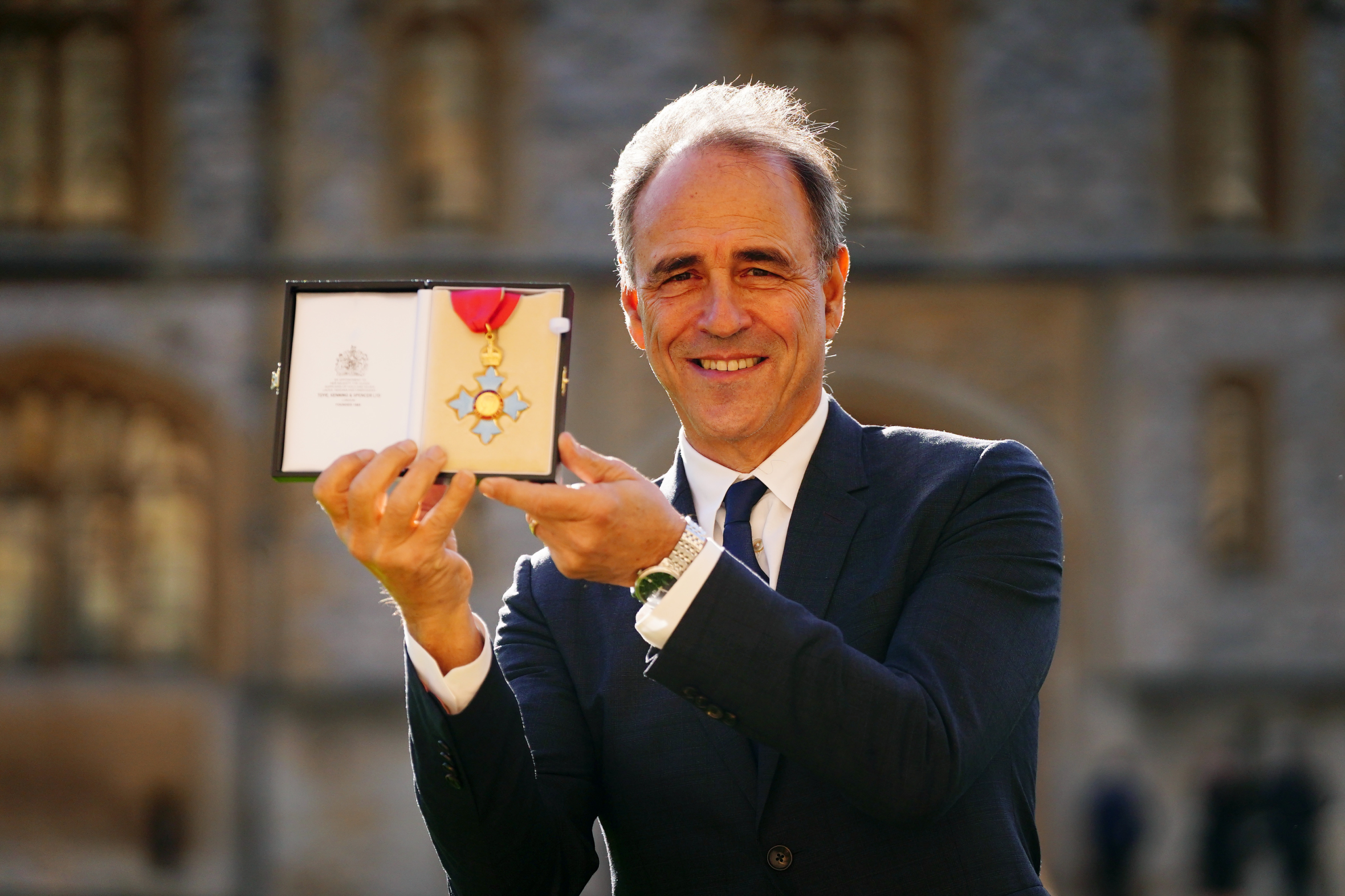 Anthony Horowitz holding up his CBE medal.