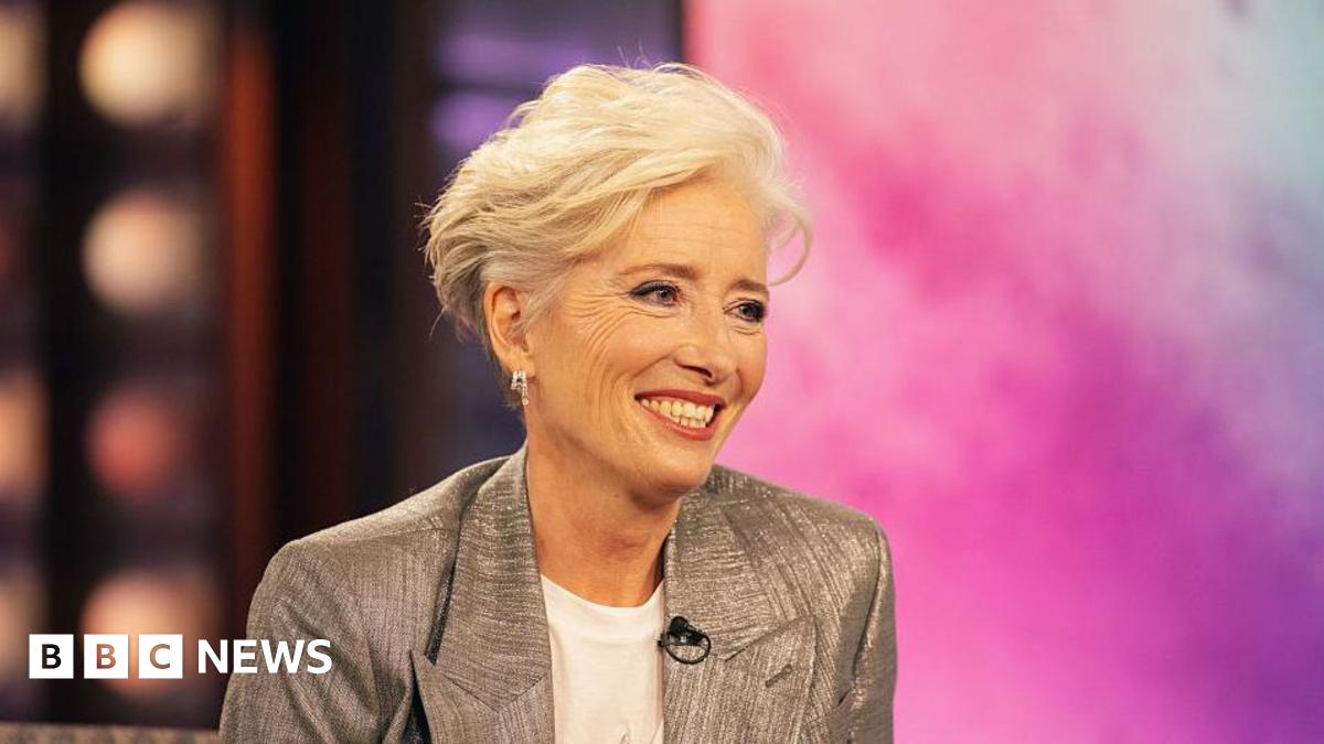 Emma Thompson sat on stage on the Kelly Clarkson show. She is smiling whilst wearing a white t-shirt and silver blazer.