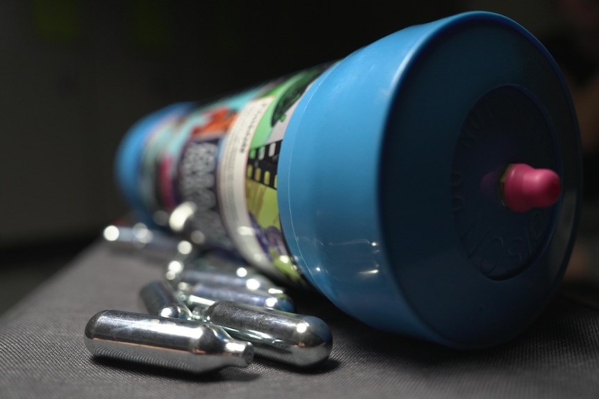 Silver cannisters of nitrous oxide in front of a colourful blue cylinder.