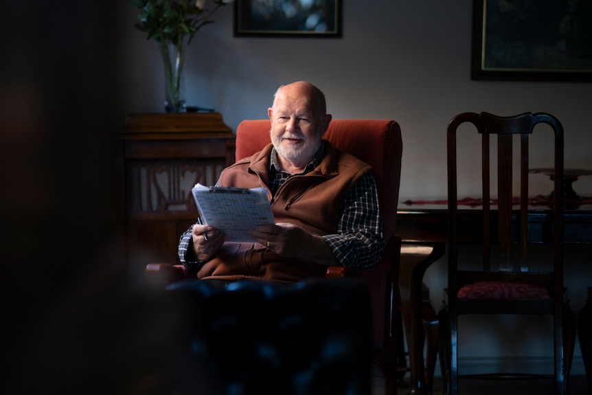 An older man smiling as he sits in his living room.