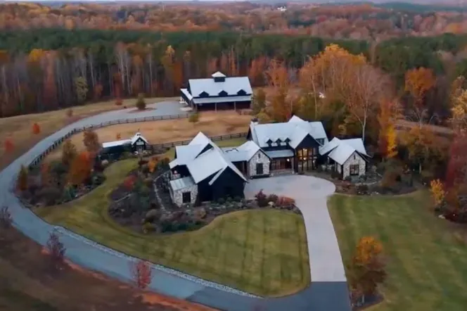 Aerial view of a sprawling estate with a large main house and a smaller outbuilding, surrounded by wooded areas with autumn foliage.