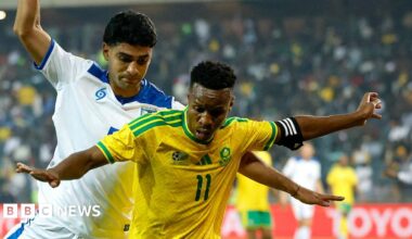 A South Africa player holds his arms out as he tries to stop a Nicaraguan player from coming up from behind him.