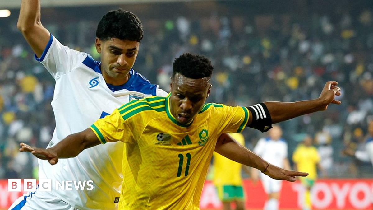 A South Africa player holds his arms out as he tries to stop a Nicaraguan player from coming up from behind him.