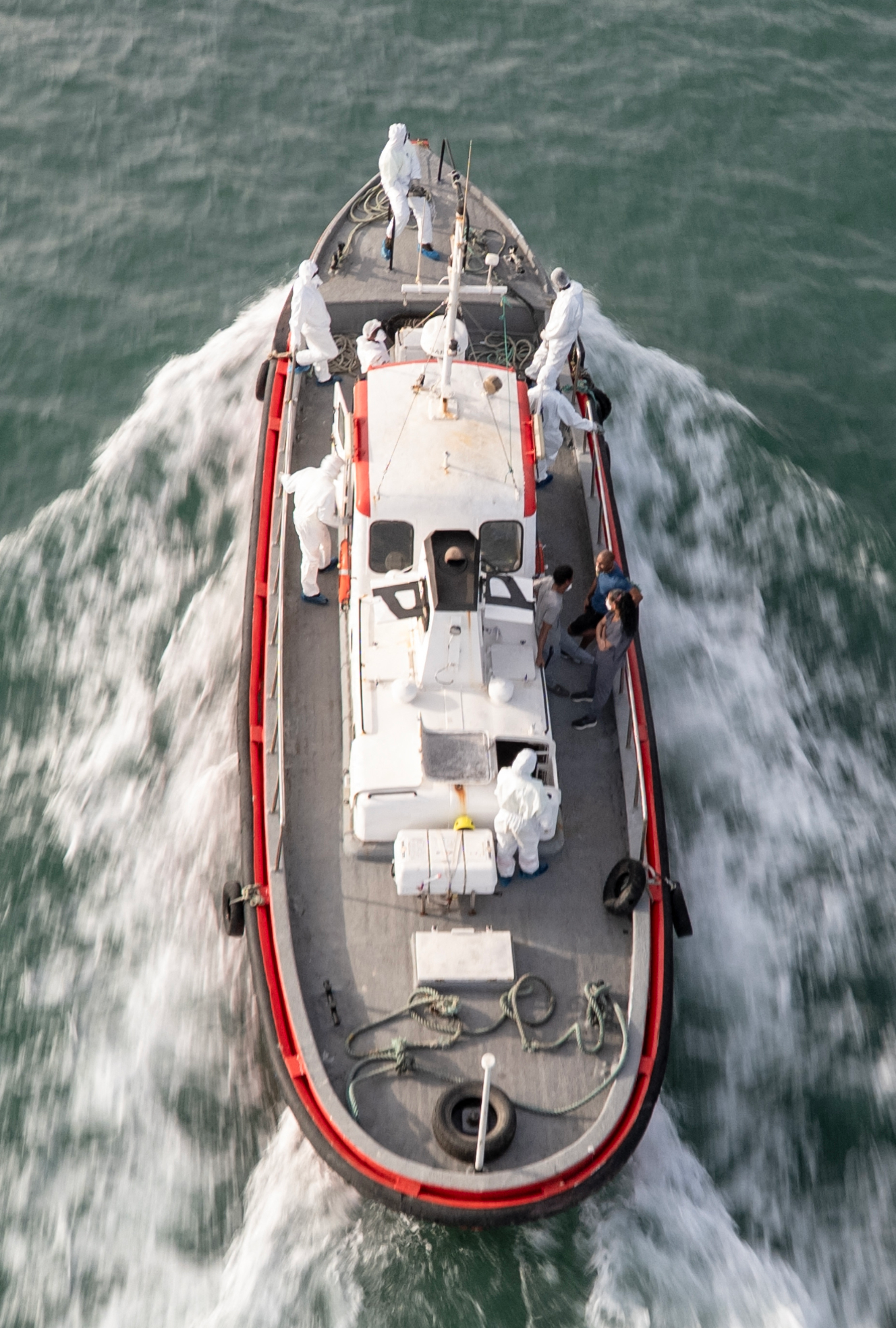 Aerial view of an ambulance boat carrying crew members in hazmat suits and others on the water.