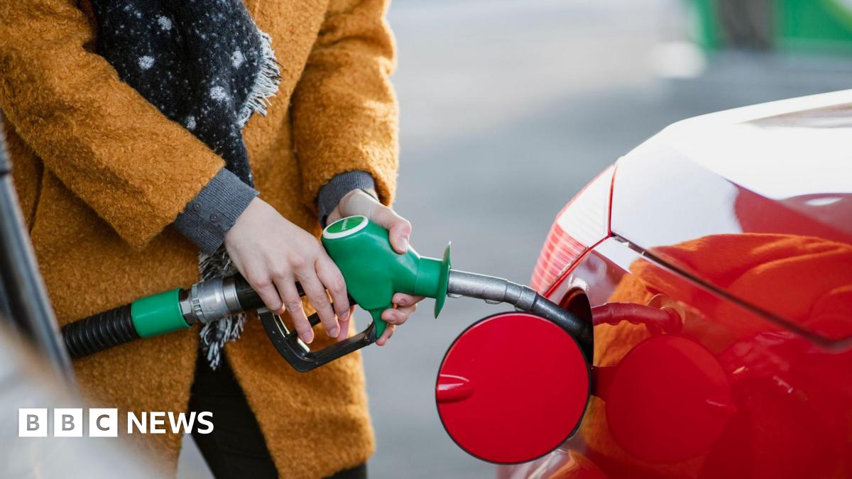 Close up shot of a young woman wearing an orange coat filling her red car with fuel.