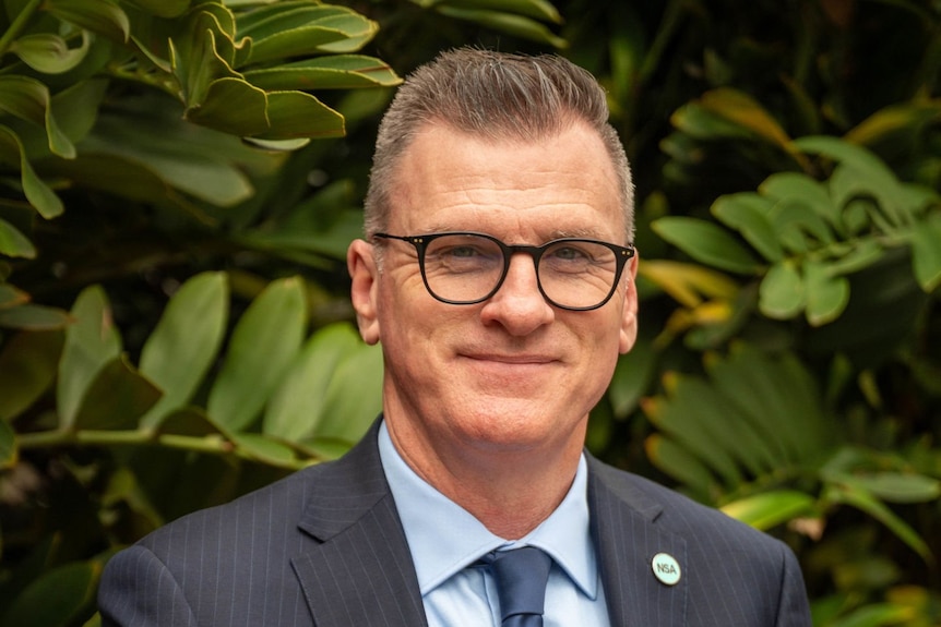Chris Grice poses for a headshot in front of a leafy hedge.