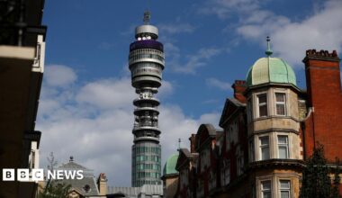 Tall slender, glass, BT Tower rises from between residential buildings