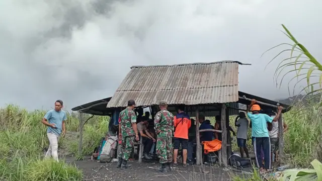 People gathering around a hut, with thick grey smoke in the background