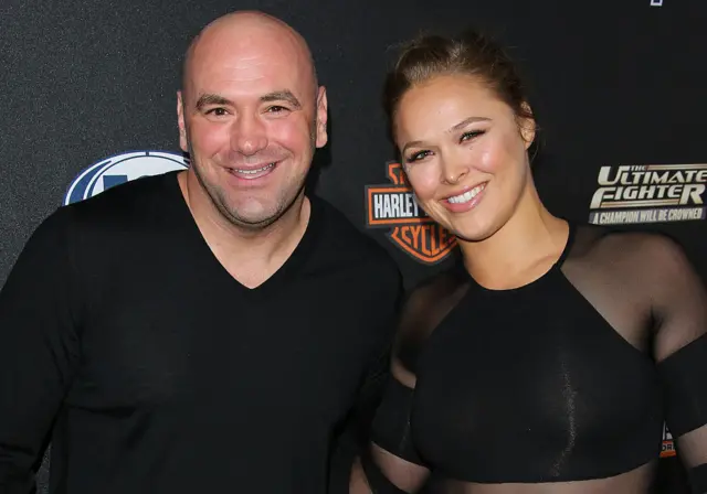 Dana White wearing a black t-shirt stands next to Ronda Rousey, who is also wearing a black top