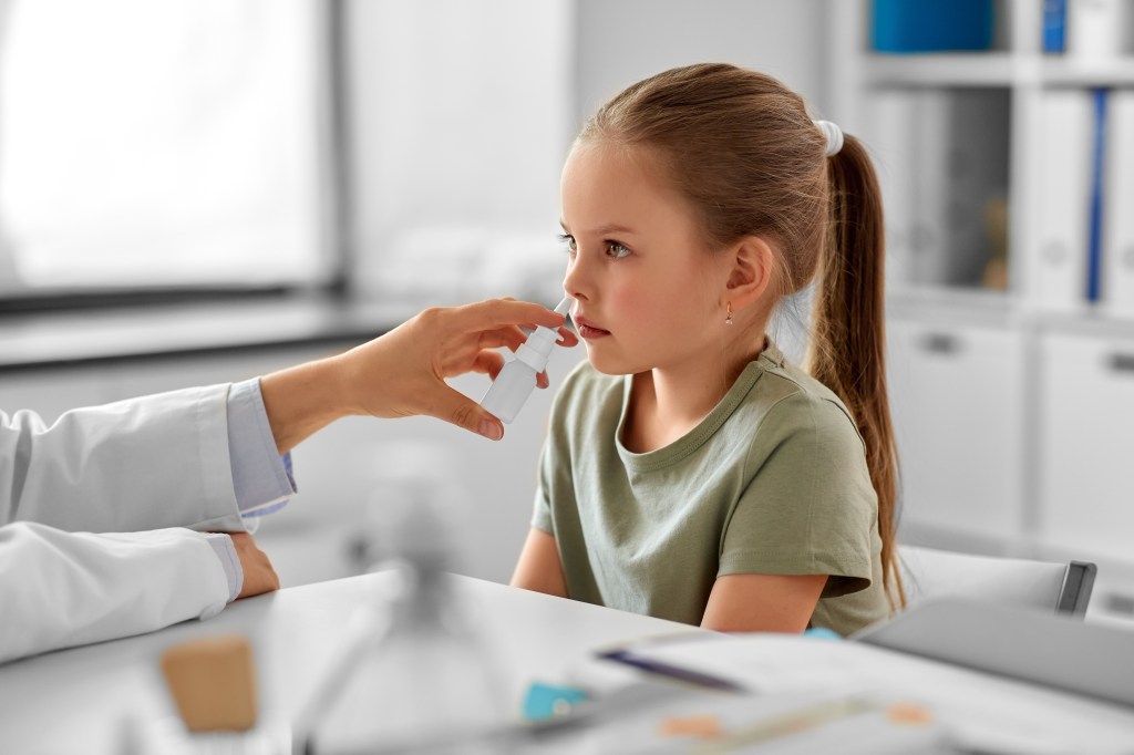 A pediatrician administers nasal spray to a young girl.