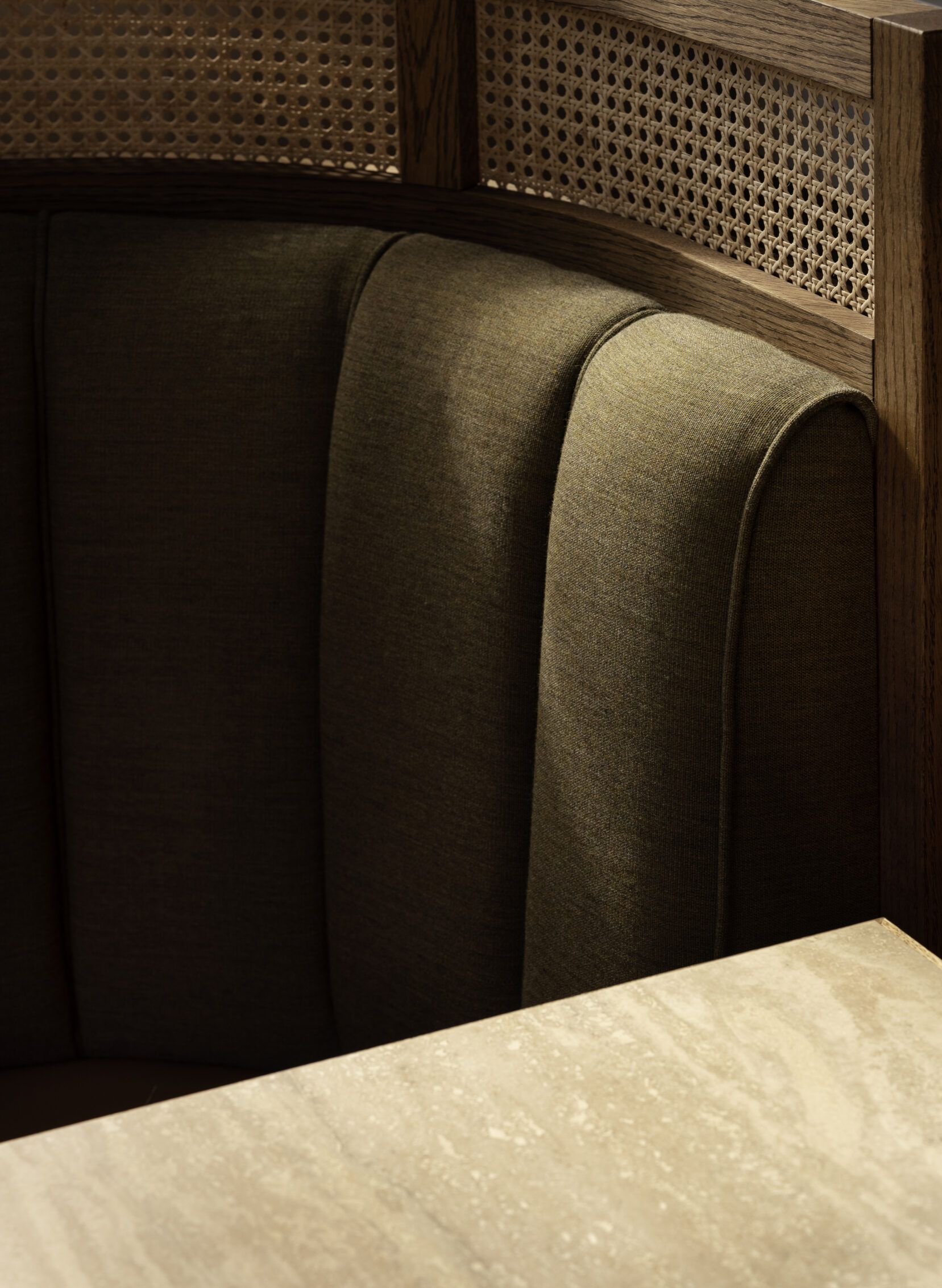 A sophisticated, retro-inspired restaurant with wood paneled walls, dark green upholstered banquettes, glazed golden tiles placed atop patterned black and white fabrics, and sculptural lights.