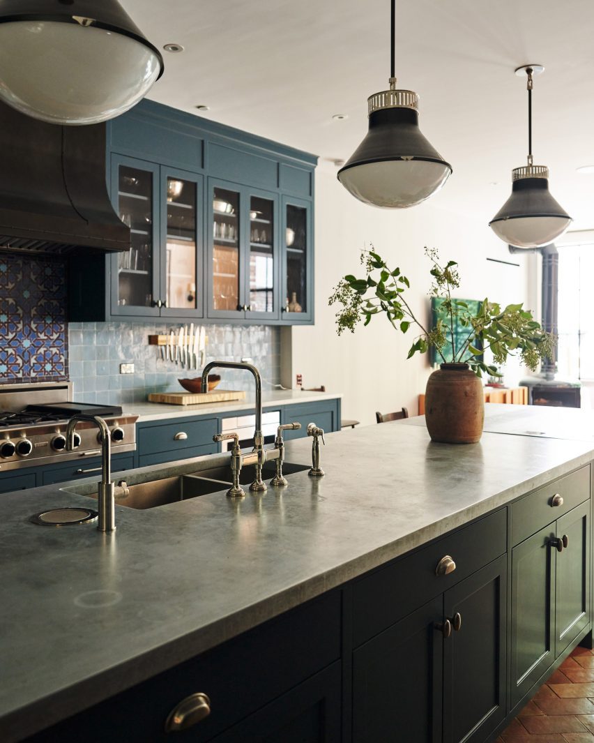 A kitchen with dark teal cabinetry and industrial lights over an island