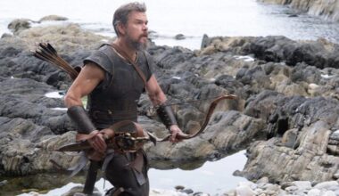 man in greek warrior garb running on a rocky beach