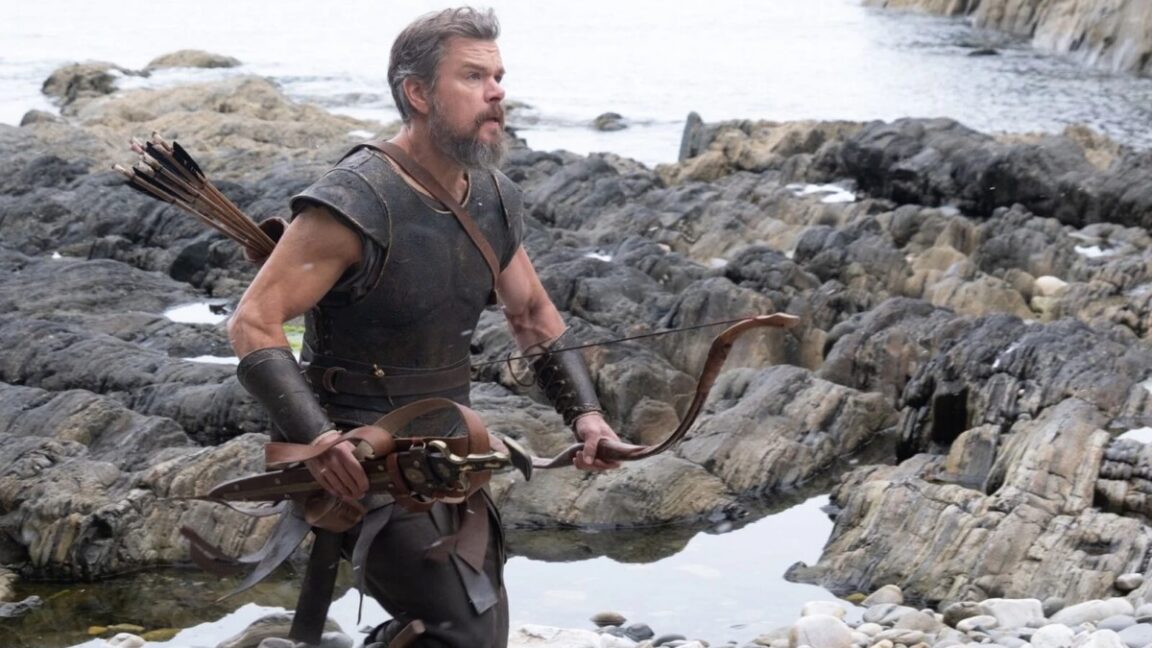 man in greek warrior garb running on a rocky beach