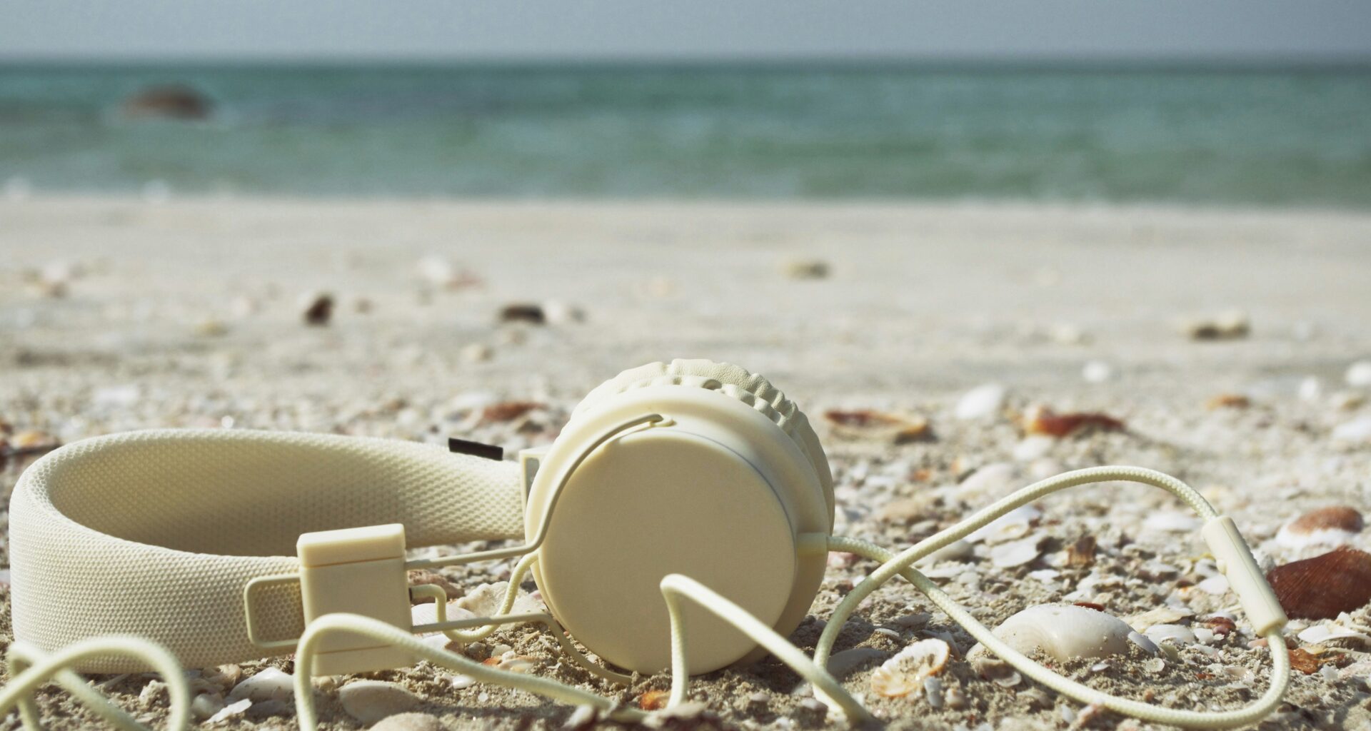 A pair of white headphones laid on the sand at the beach