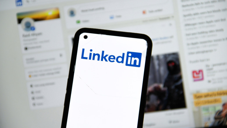 The LinkedIn logo on a phone screen with the LinkedIn website in the background.