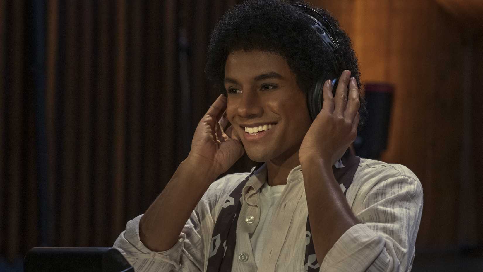 Jaafar Jackson as Michael Jackson smiling while wearing headphones in Michael