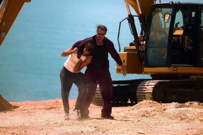 jacob-elordi-matthew-willig Nate is held in a headlock by Artur in a desert setting, with a mechanical digger parked behind them
