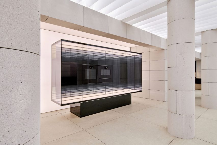 Glass display case presenting Gaggenau appliances within a softly lit stone interior