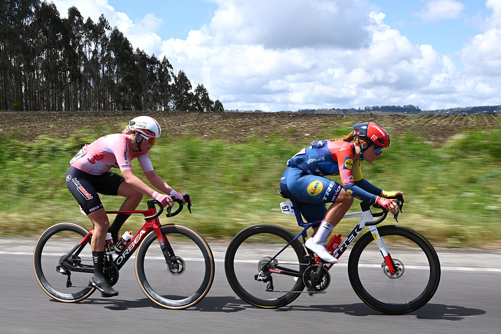 Sterre Vervloet and Felicity Wilson-Haffenden riding along a grassy field with trees and blue sky in the distance