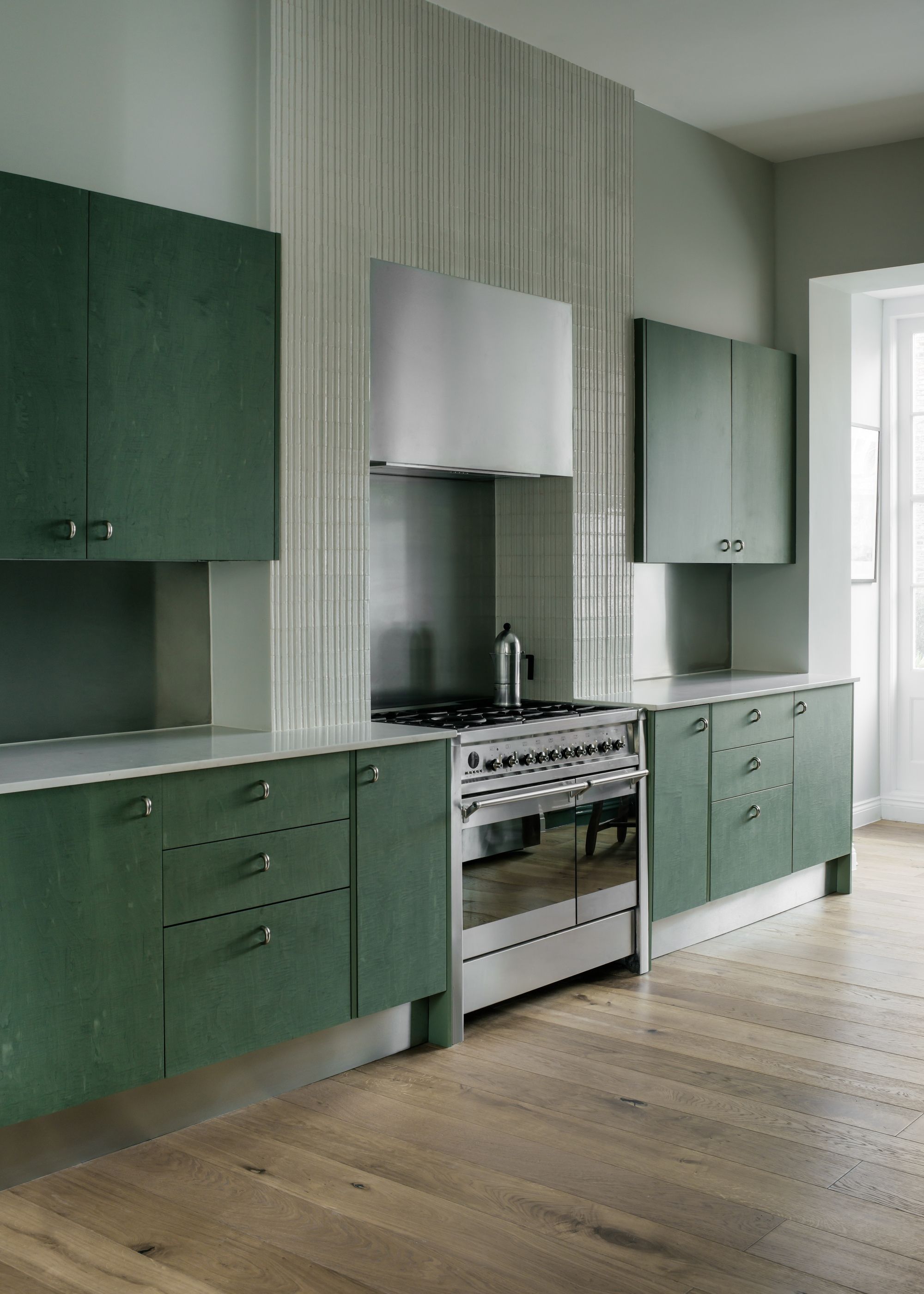 Image of a green kitchen with dark, teal-tinted green cabinets with powder green-blue walls and wooden floors.